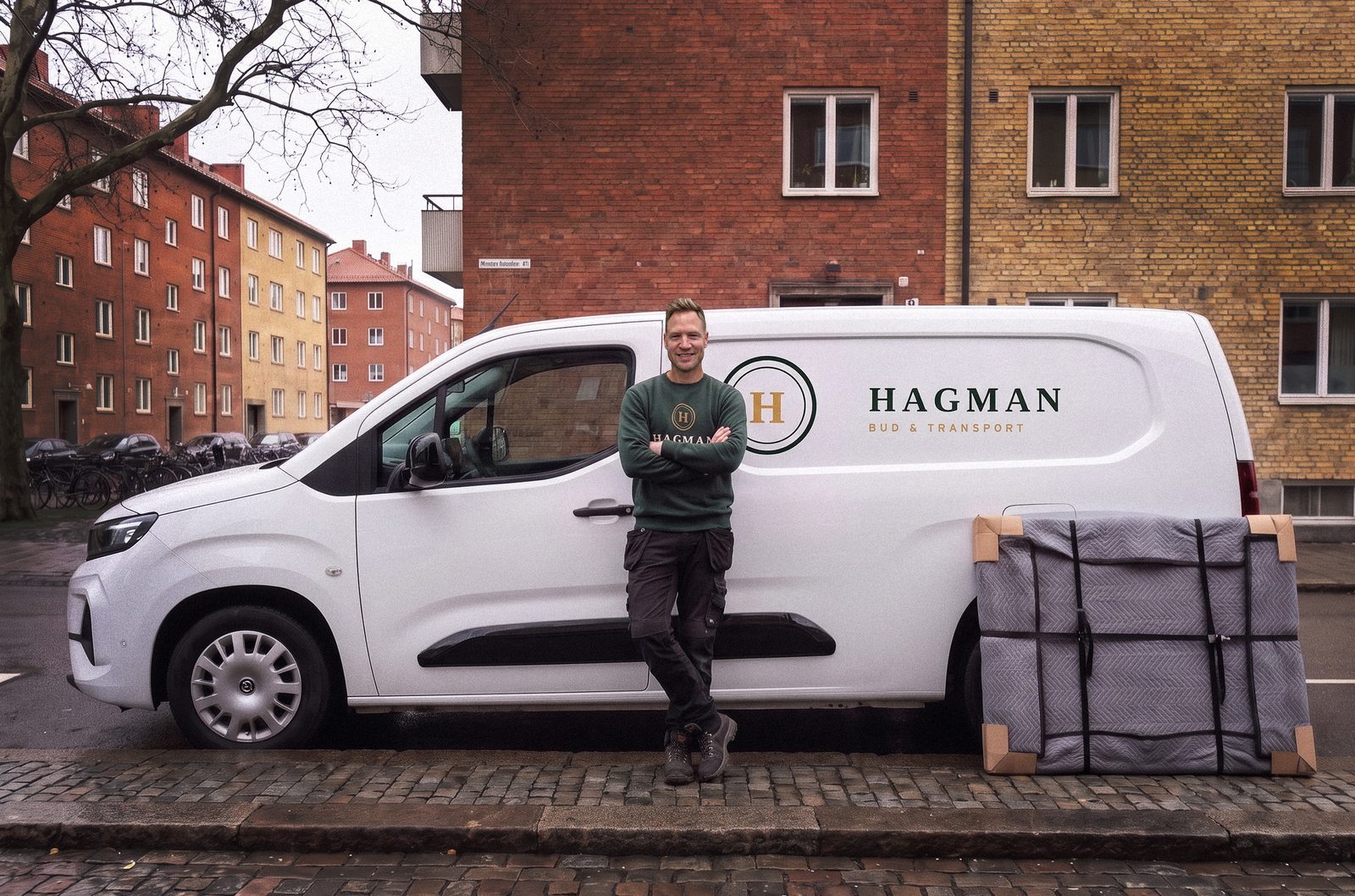 Andreas Hagman står med armarna i kors lutad mot Hagmans skåpbil, bredvid ett emballerat föremål på gatan